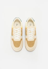 Beige and cream sneakers with perforated detailing, white laces, and colorful accents of orange and blue on the side. Green heel tab.
