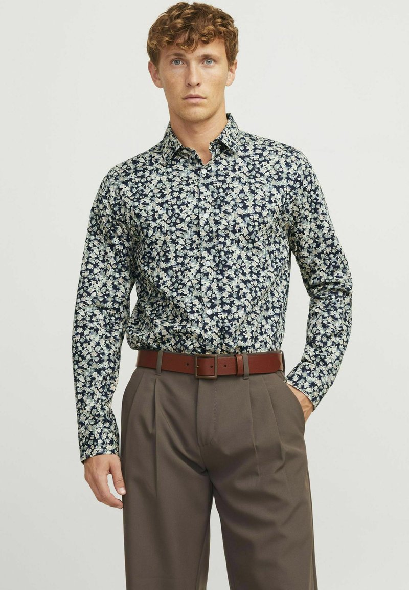Chemise à manches longues marine foncé avec un imprimé floral blanc et bleu clair. Associée à un pantalon marron et une ceinture assortie.