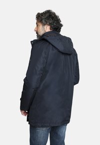 Chaqueta acolchada azul marino con capucha, que presenta una textura suave, bolsillos con botones y un diseño de longitud media, vista desde la parte posterior.