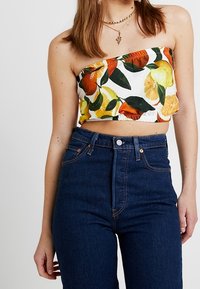 Top corto senza spalline in tessuto bianco con motivi di arance e limoni, abbinato a jeans scuri a vita alta.