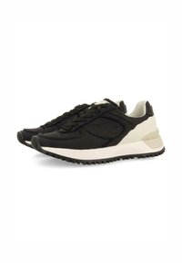 Zapatillas de running negras y crema con una parte superior de tela suave, cordones planos y una suela de goma texturizada para mayor agarre. Acentuadas con un talón de color claro.