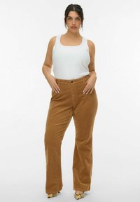 Pantaloni a zampa d'elefante in corduroy marrone con vita alta e chiusura a bottoni, abbinati a un top senza maniche bianco, che mostra una trama liscia.