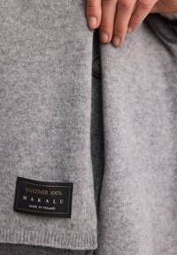 Szary kardigan z kaszmiru o gładkiej fakturze, z zapięciem na guziki i metką z napisem "KASZMIR 100% MAKALU MADE IN POLAND."