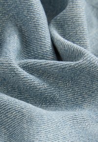Tissu en denim bleu clair avec une texture douce, motif de sergé visible et plis légers indiquant la chute et la souplesse.