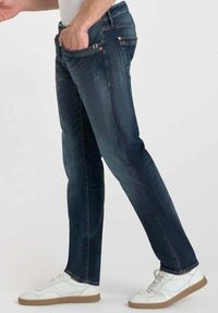Jeans de mezclilla azul oscuro con un diseño de pierna recta, con un ligero desvanecimiento, bolsillos frontales y costuras de cobre, combinados con zapatillas blancas.