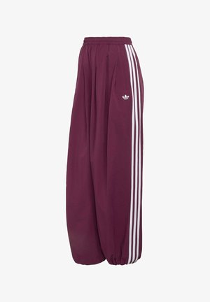 Pantalones deportivos Adidas de pierna ancha en color púrpura, con cintura y puños elásticos, detalles de tres franjas blancas a lo largo de los costados y un pequeño logo en el muslo.