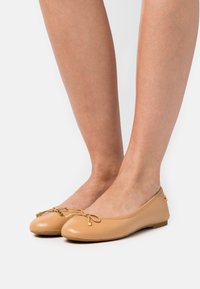 Ballerine in pelle beige con punta rotonda, dettagli decorativi a forma di fiocco e piccoli accenti dorati. Texture liscia, suola piatta.