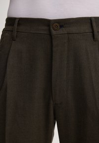 Ciemnozielone spodnie wykonane z teksturowanej tkaniny, z zapięciem na guzik, paskami do pasa i kieszeniami bocznymi, o dopasowanym kroju.