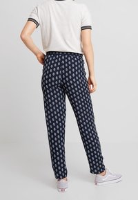 Granatowe spodnie z białym wzorem marynistycznym, o prostym kroju, z elastycznym paskiem w talii i lekkiego materiału, zestawione z szarą koszulką w paski i sneakersami.