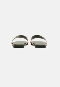 Sandali piatti neri con un design minimalista, caratterizzati da cinturini curvi e una soletta testurizzata per il comfort. Dettagli in rosso e bianco visibili.