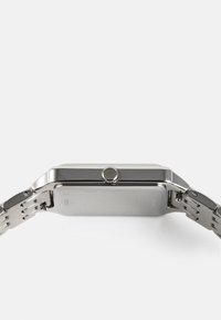 Montre en acier inoxydable argenté avec un boîtier rectangulaire, une couronne texturée et un bracelet à maillons. Dos plat avec des détails gravés.