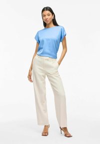 Top corto de satén azul de manga corta combinado con pantalones anchos crema, con un acabado texturizado y un ajuste relajado. Los stilettos completan el look.