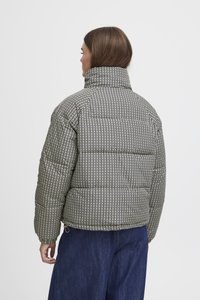 Puffersjakke med et svart og hvitt houndstooth-mønster, høy krage og quiltet tekstur. Kombinert med marineblå vide bukser.