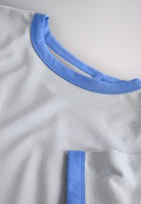 Light gray fabric shirt with blue round neckline and blue trim on visible front pocket.