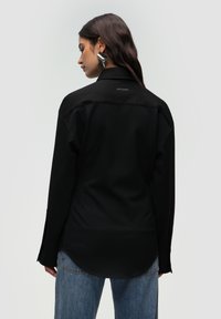 Sort langærmet skjorte med en rund kant, lavet af glat stof, med et lille logo på ryggen, parret med lyseblå jeans.