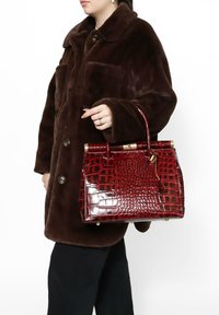 Borsa a tracolla rossa con stampa coccodrillo, dalla forma strutturata, con hardware dorato e manico superiore, abbinata a un cappotto di pelliccia marrone.