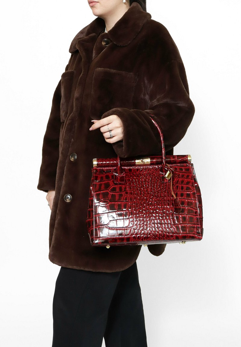Borsa a tracolla rossa con stampa coccodrillo, dalla forma strutturata, con hardware dorato e manico superiore, abbinata a un cappotto di pelliccia marrone.