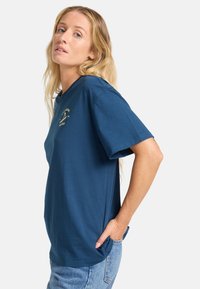 Blå bomulds T-shirt med korte ærmer, rund halsudskæring, med et lille gult grafik på venstre bryst og en afslappet pasform.
