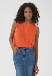Top naranja sin mangas con escote en V y tejido texturizado, combinado con una falda de mezclilla azul de cintura alta.