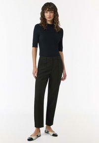 Czarny top z krótkim rękawem i okrągłym dekoltem, w zestawieniu z ciemnozielonymi spodniami o dopasowanym kroju, które mają wyprasowane przody oraz eleganckie czarno-białe baleriny.