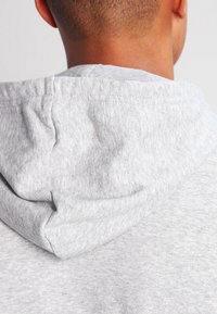 Hoodie en coton gris avec une texture douce, doté d'une capuche à cordon de serrage. Le tissu présente un motif chiné subtil.