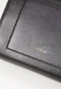 Zwarte leren portemonnee met een gestructureerd oppervlak, gouden "Furla" logo en zichtbare stiksels langs de randen. Compacte en rechthoekige vorm.