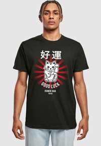 Zwarte katoenen T-shirt met een ontwerp van een witte cartoonkat met rode stralen, tekst met "GOOD LUCK RAMEN BAR TOKYO" en een speelse kattenhouding.
