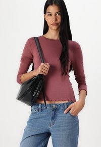 Langermet, ribbet maroon topp med scalloped kant, parret med høyt liv lyseblå jeans. Modellen holder en svart, myk veske.