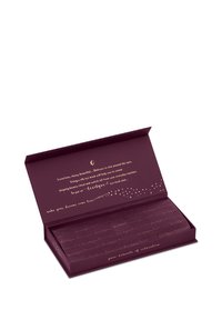 Open donkere paarse doos met gouden tekst die een zijden oogmasker voor de gevoelige huid beschrijft, met sterren- en maansikkelontwerp binnenin het deksel.