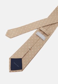 Cravate beige à motif avec des rayures diagonales et des points blancs. Section arrière bleu marine avec une étiquette indiquant "MICHAEL KORS". Tissu texturé.