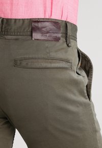 Olivgrüne Baumwollhose mit einem braunen Lederschild. Sie verfügt über eine einzelne Gesäßtasche und eine glatte Textur, die für eine lockere Passform sorgt.