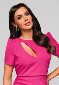 Robe fuchsia avec des manches bouffantes et un décolleté ajouré. Tissu lisse, silhouette ajustée, accentuée par des boucles d'oreilles en strass circulaires.