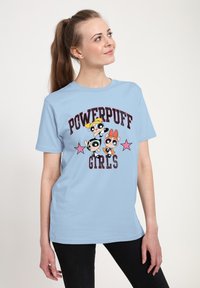 Světle modré bavlněné tričko s grafikou "Powerpuff Girls", se třemi postavami a růžovými hvězdami. Krátké rukávy a kulatý výstřih.
