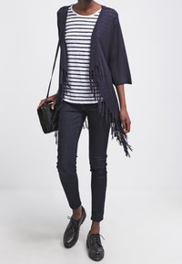 Námořnický kardigan s třásněmi, pruhované bílé a námořnické tričko, tmavé úzké džíny a černé boty, doplněné černou kabelkou.
