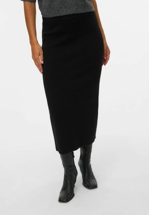 Jupe tricotée noire, mi-longue, avec une silhouette ajustée, une texture douce et un léger stretch, assortie à des bottes noires montantes.