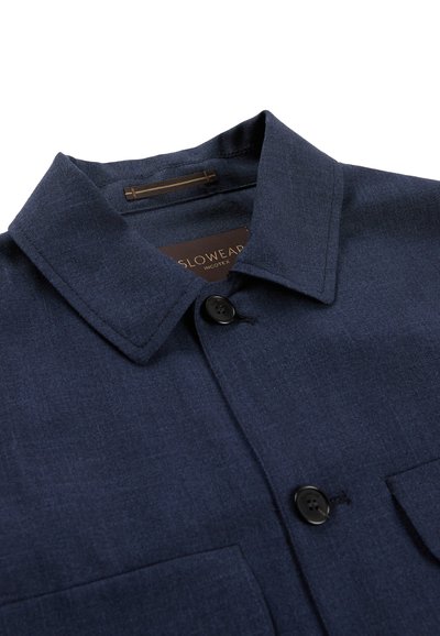 Granatowa koszula z kołnierzykiem, czarnymi guzikami, dwoma kieszeniami na piersiach i widoczną metką marki po wewnętrznej stronie kołnierza.