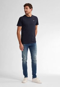 Tricou din bumbac albastru marin, cu mâneci scurte și decolteu rotund, asortat cu blugi bleu și adidași albi, având un mic logo pe piept.