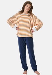 Gestreiftes orange-weißes, oversized Fleecepullover mit langen Ärmeln, kombiniert mit weichen, marineblauen Fleecepantalons. Es zeichnet sich durch eine entspannte Passform und weite Bündchen aus.