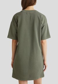 Olive green cotton t-shirt dress with short sleeves, rounded neckline, and a relaxed fit, featuring a smooth texture and simple design.