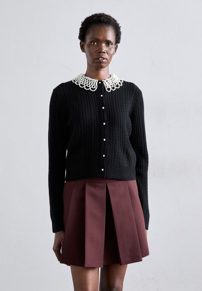 Cardigan noir en tricot torsadé avec un col en dentelle blanche, ornée de boutons en perles. Assorti à une jupe plissée bordeaux. Design simple et structuré.