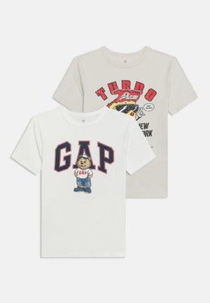 Deux t-shirts à manches courtes pour enfants : blanc avec un ours et les lettres « GAP », beige avec un motif pizza de course et le texte « TURBO ».