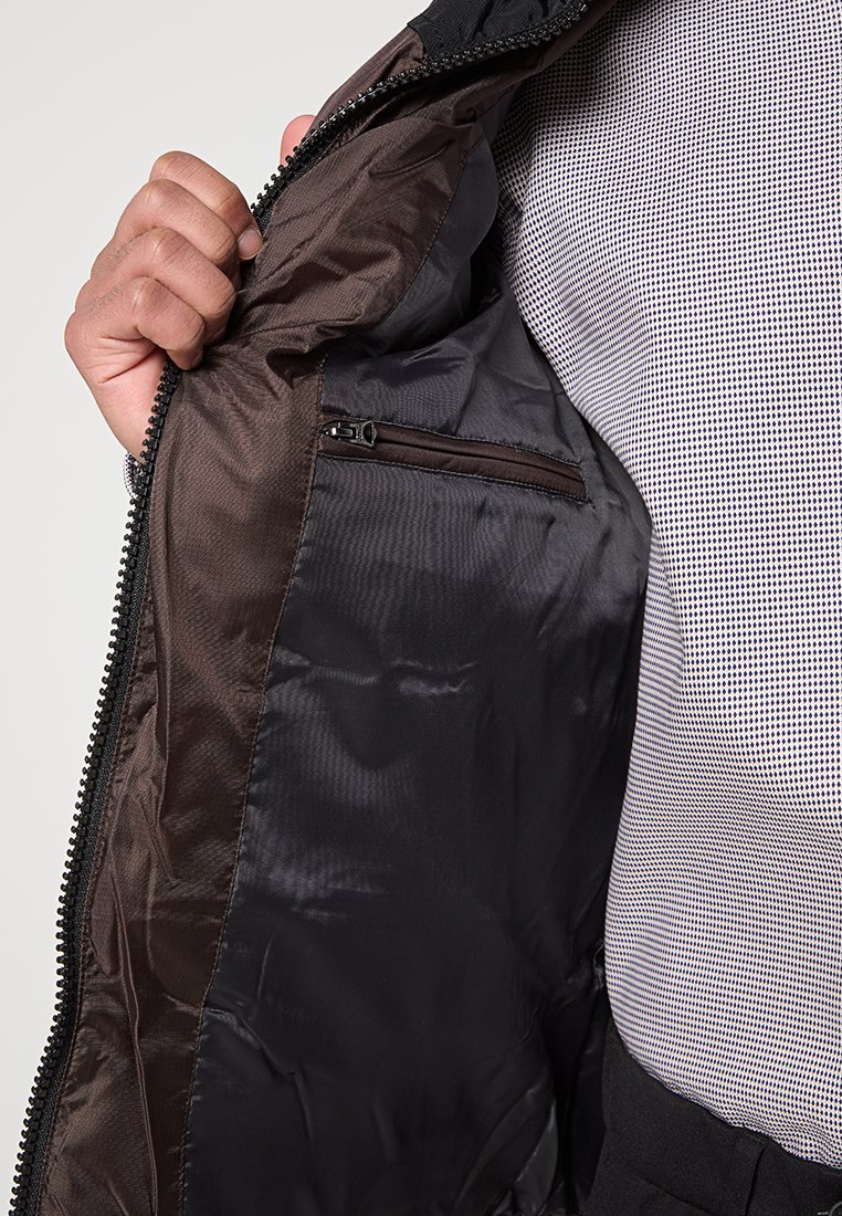 Veste noire avec une doublure intérieure lisse et brillante et une poche zippée. Le tissu extérieur est texturé, mettant en avant un gros plan du design intérieur.