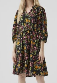 Květinové šaty s černým pozadím, výstřihem do V a balónovými rukávy. Obsahují barevné květiny v růžové, žluté a zelené. Design se staženým pasem.