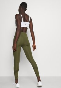 Witte sport-bh met verstelbare bandjes en zwarte accenten, gecombineerd met hooggesneden olijfgroene leggings met een gestructureerd patroon en enkelmanchetten.