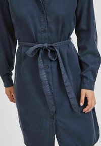 Mörkblå skjortklänning i mjukt tyg, med knäppning fram, långa ärmar och ett knytbälte vid midjan. Inkluderar sidofickor och en avslappnad passform.