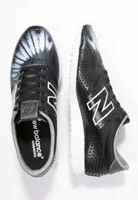 Baskets noires et grises avec un motif tie-dye, dessus en maille, texture perforée, semelles blanches et logo blanc "N" prominent.