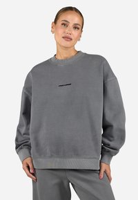 Grå oversized sweatshirt laget av mykt stoff, med rund hals og ribbestrikkede mansjetter. 'PEAC1000' logo i svart på brystet.