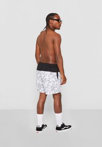 Svart-hvite blomsterbadedraktshorts med svart liv, brukt med svarte Vans-sko og hvite sokker, sett fra baksiden.