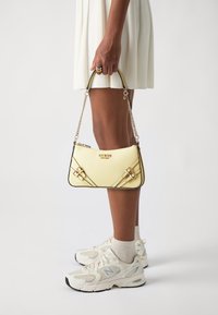 Yellow handbag with textured finish, featuring a black trim and gold hardware. It has a chain strap and decorative straps across the front.