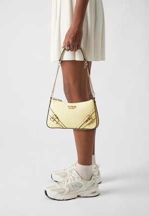 Keltainen käsilaukku, jossa on teksturoidu pinta, musta koristekulmaviimeistely ja kultaiset metalliosat. Laukussa on ketjuhihna ja koristeelliset hihnat edessä.